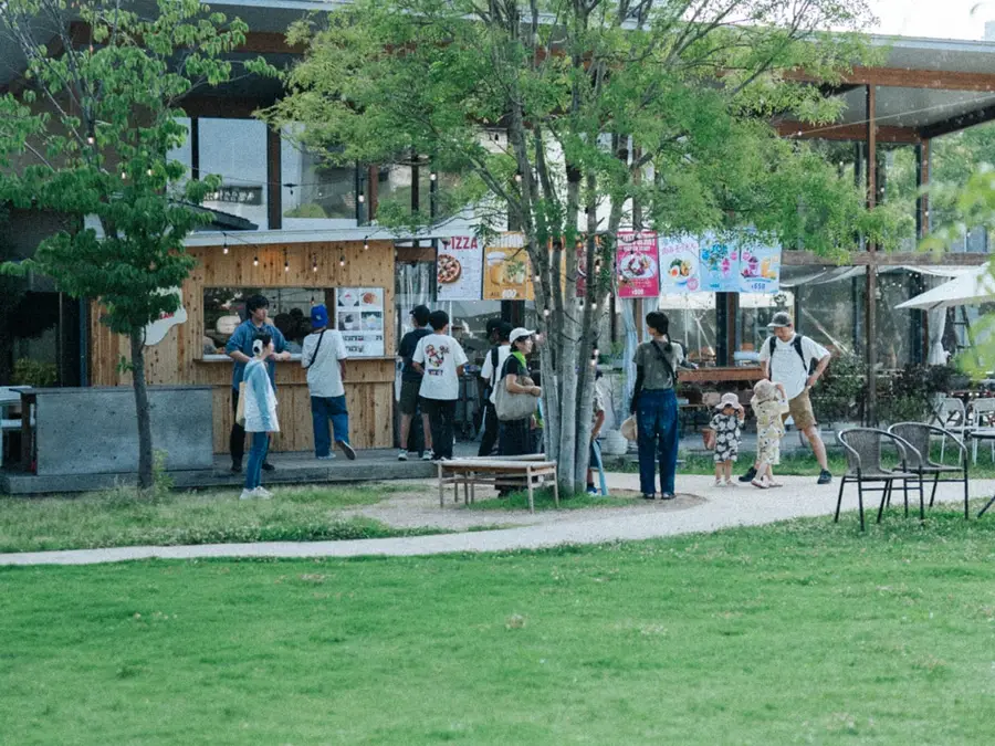 昼間の福山中央公園。広い芝生の奥に、ガーデンレストランと出店のテントが並んでいる。
