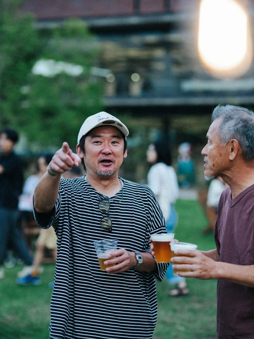 夕暮れの芝生の広場で、生ビールのカップを手に笑顔で語らう2人の来場者。